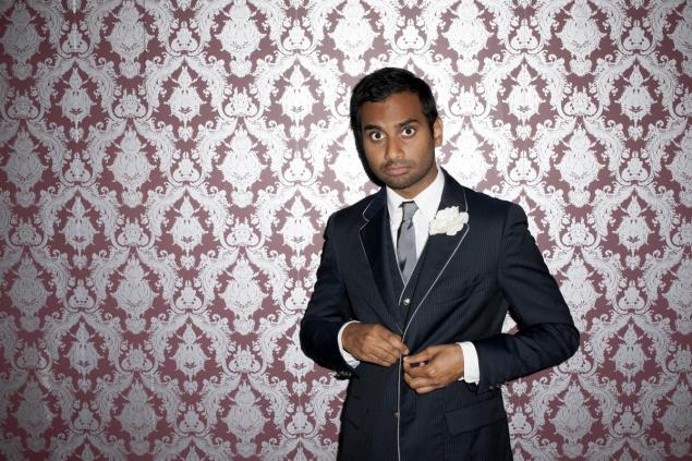 Author Aziz Ansari posing next to patterned wallpaper photo